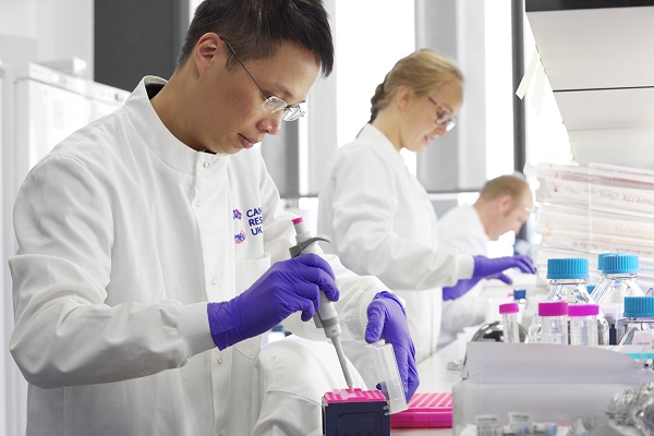 Researcher in a white lab coat pipetting in a lab